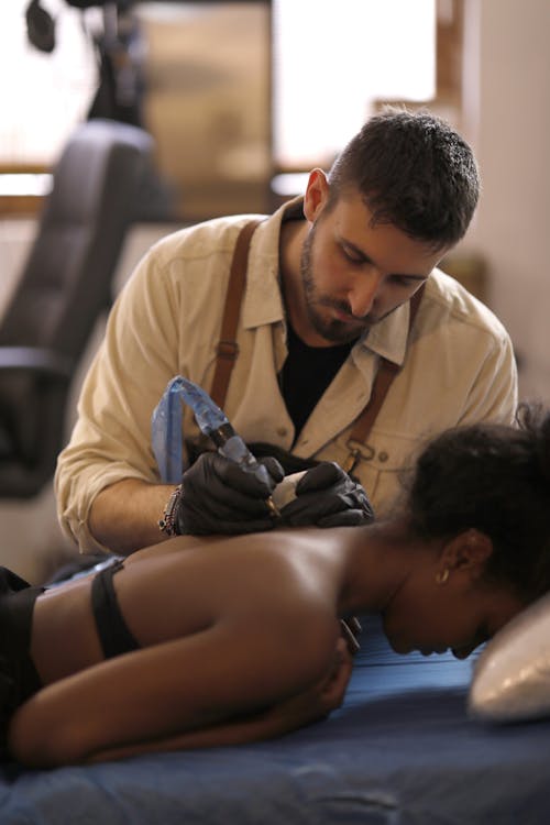Man in Beige Button Up Shirt Tattooing A Woman On Her Back