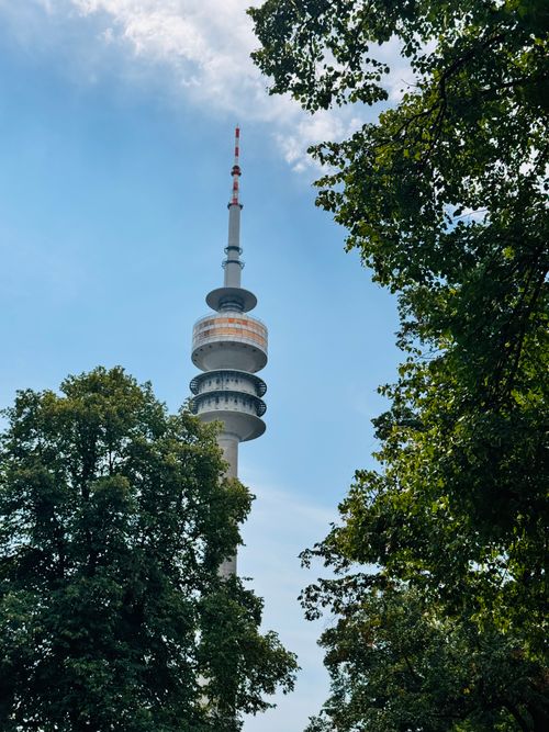 Free View of the Olympic Tower in Munich surrounded by lush green trees under a clear blue sky. Stock Photo