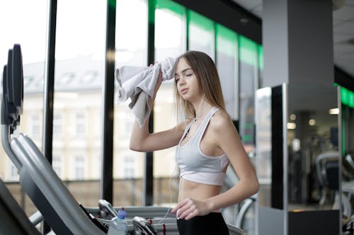 Free Woman in White Tank Top Wiping Her Sweat With Towel Stock Photo