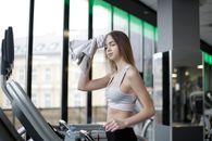 一位年轻女子在室内跑步机上边听音乐边锻炼，以保持健康