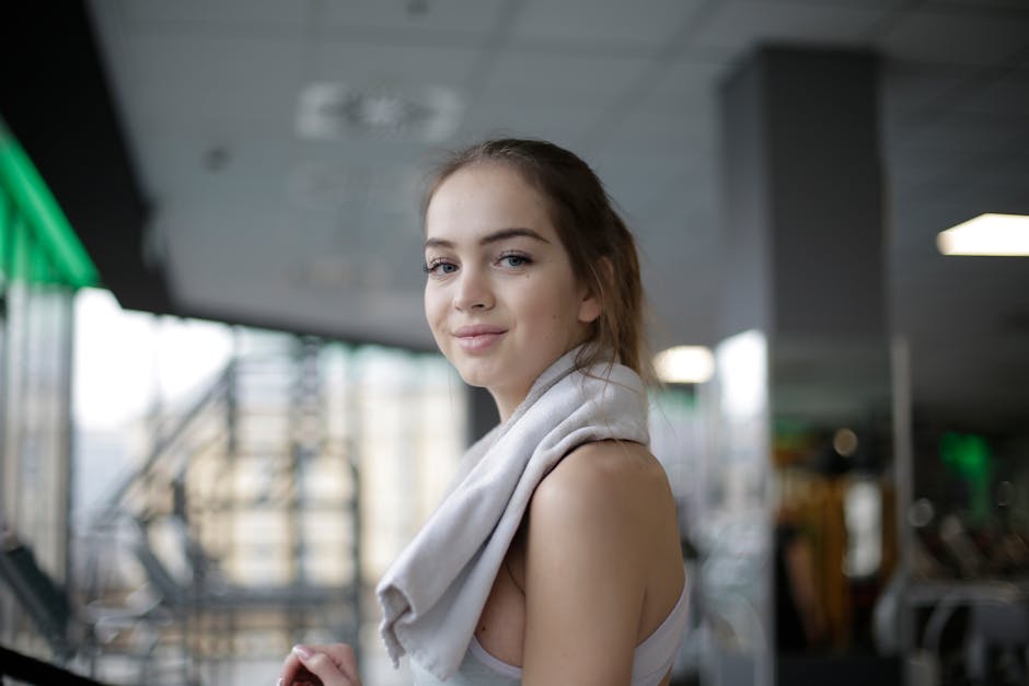 Portrait of a smiling woman with a towel over her shoulder in a modern gym, exuding confidence.