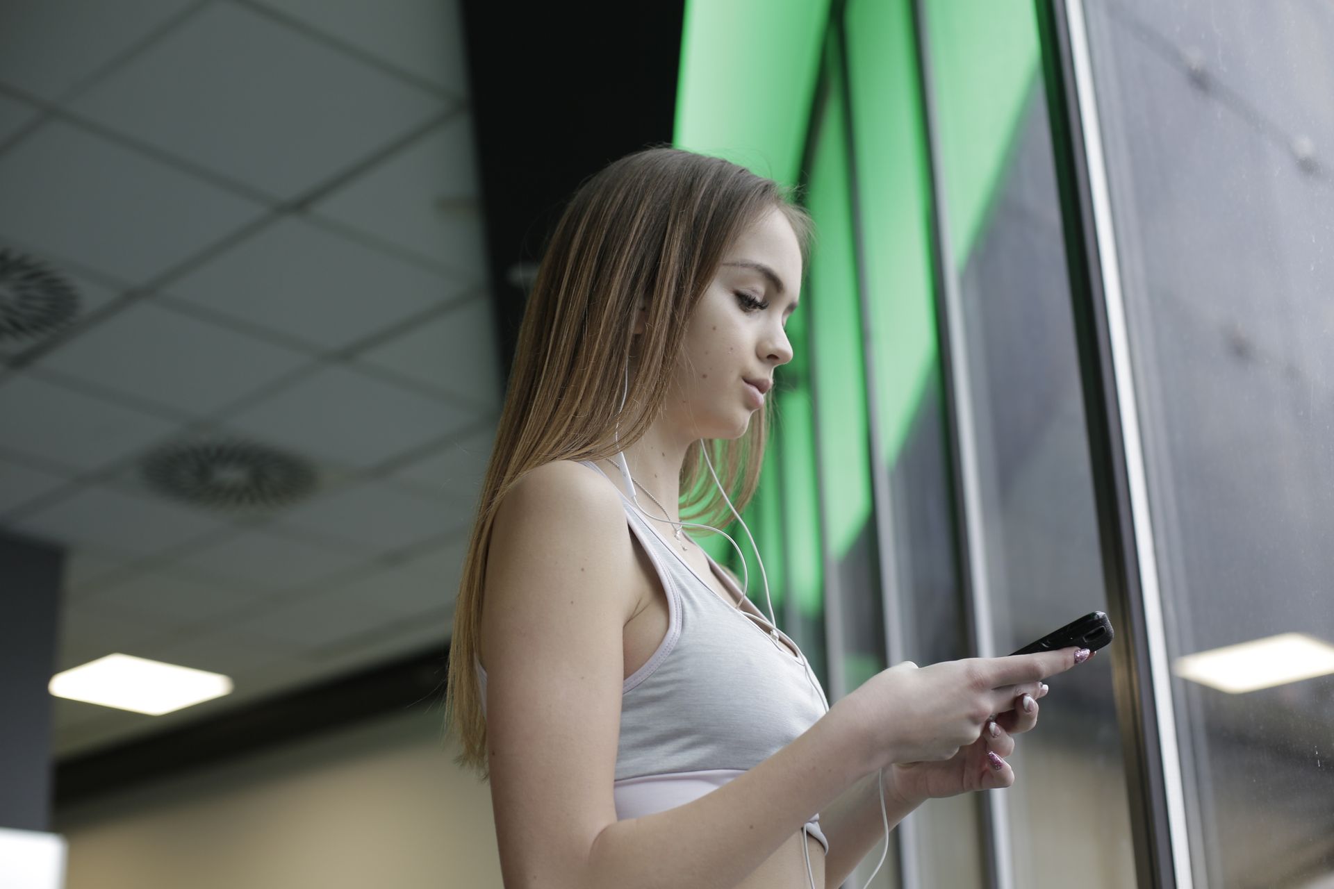 Young woman listening to music on her smartphone by a window indoors.