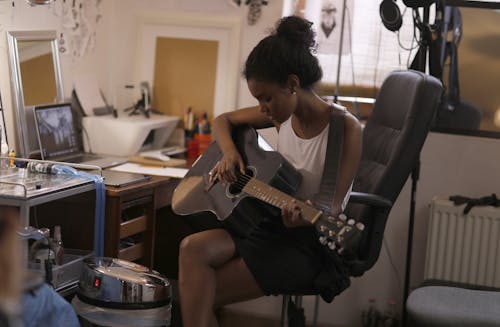 Woman in White Tank Top Playing An Accoustic Guitar