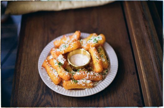 Plate of crispy fried cheese sticks garnished with herbs and cheese, served with dipping sauce.