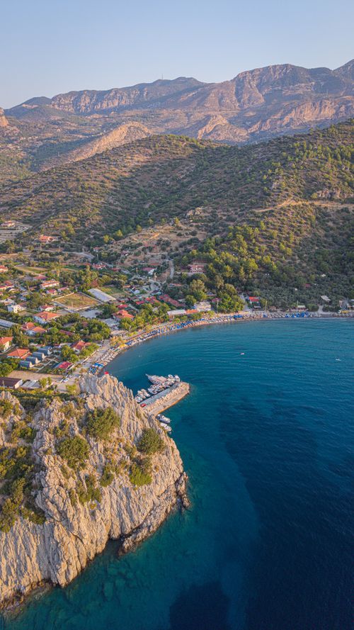 Free Breathtaking aerial view of a coastal village by a vibrant blue sea and lush hills. Stock Photo