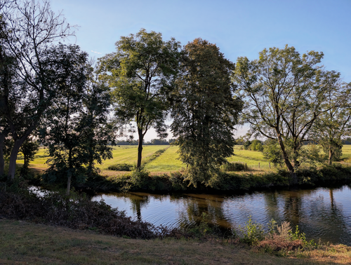 Free Tranquil countryside scene with green fields and a calm river. Stock Photo