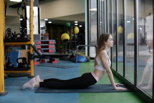 A young woman in yoga attire performs a cobra stretch in a well-equipped gym.
