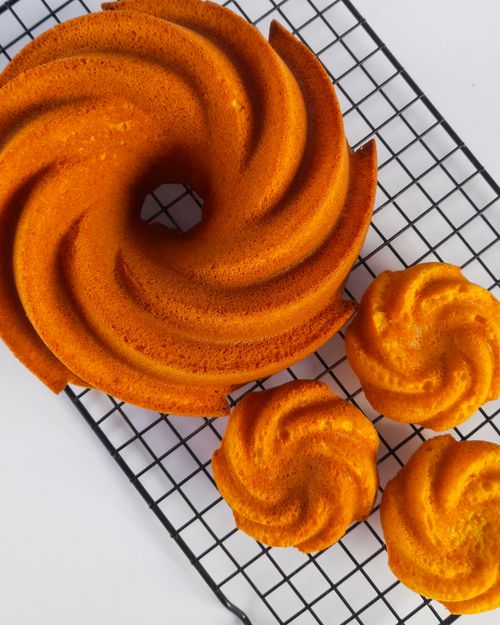Free Top view of a beautifully spiral-shaped bundt cake and mini cakes on a cooling rack. Stock Photo