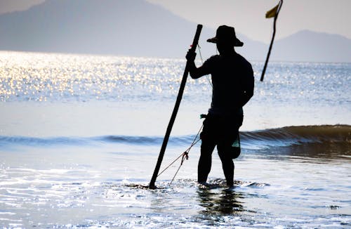 Mann, Der Auf Flachem Wasser Des Strandes Gegen Das Lichtfoto Während Des Tages Fischt