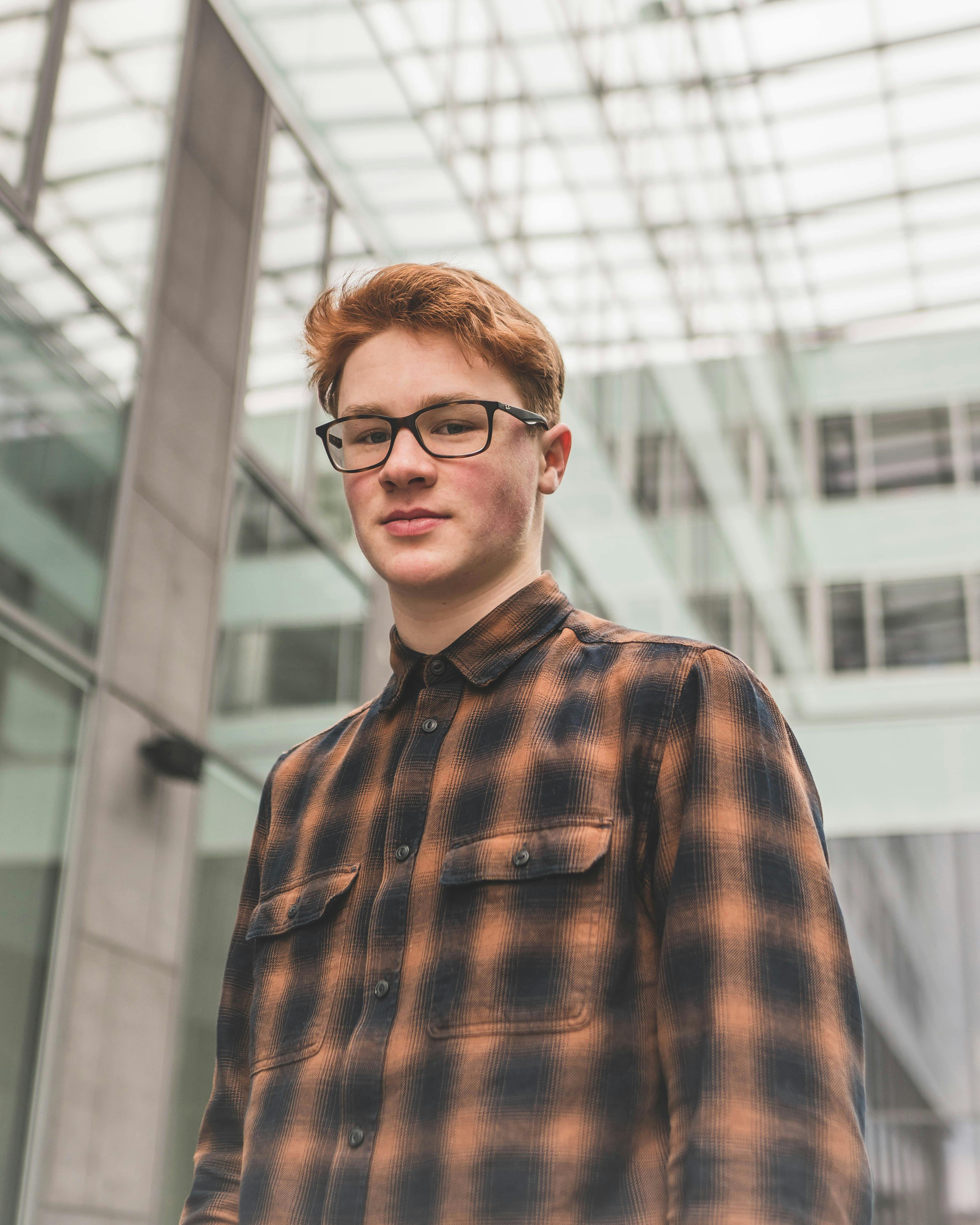 一位戴着眼镜、穿着格子衬衫的年轻人，站在现代中庭的肖像