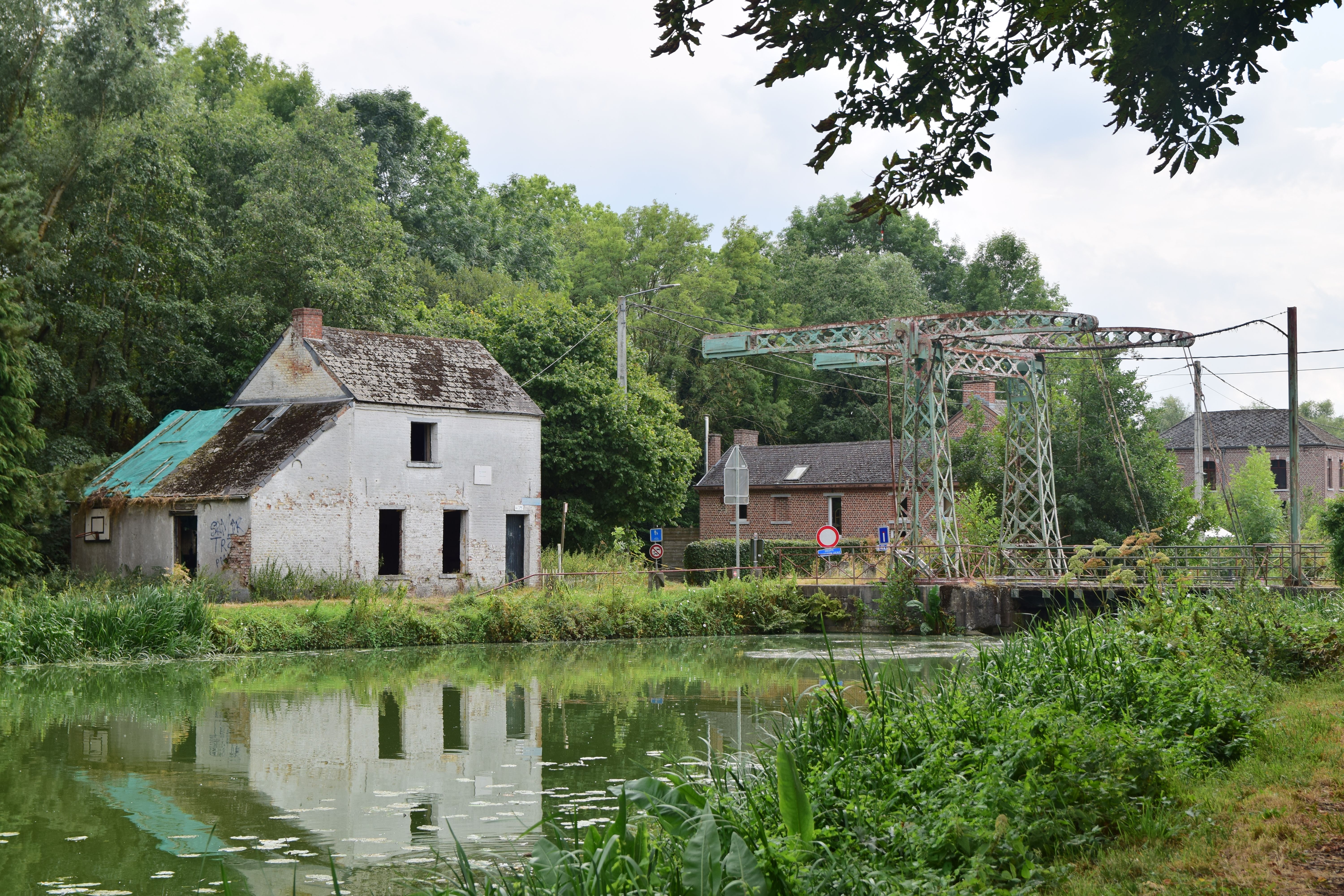 Scenic view of an old stone house and bridge over a tranquil canal in a lush green landscape.