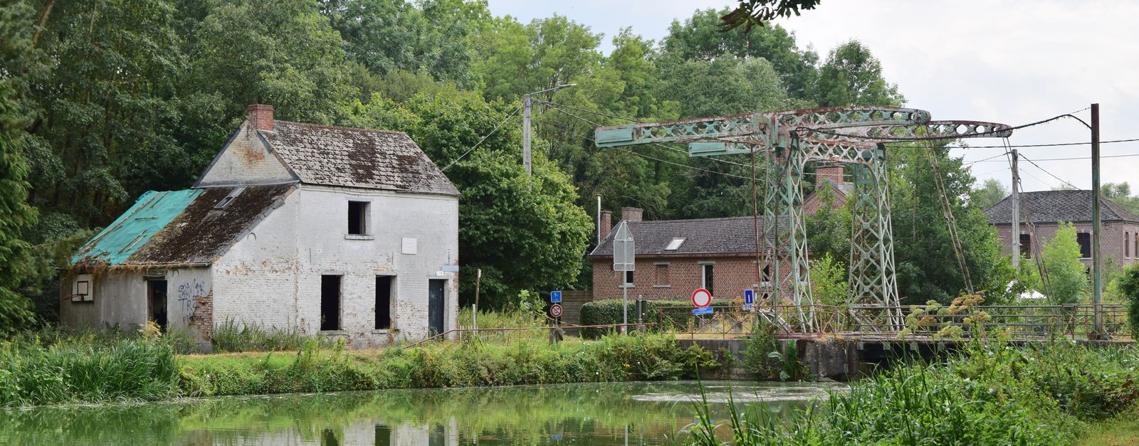 Scenic view of an old stone house and bridge over a tranquil canal in a lush green landscape.