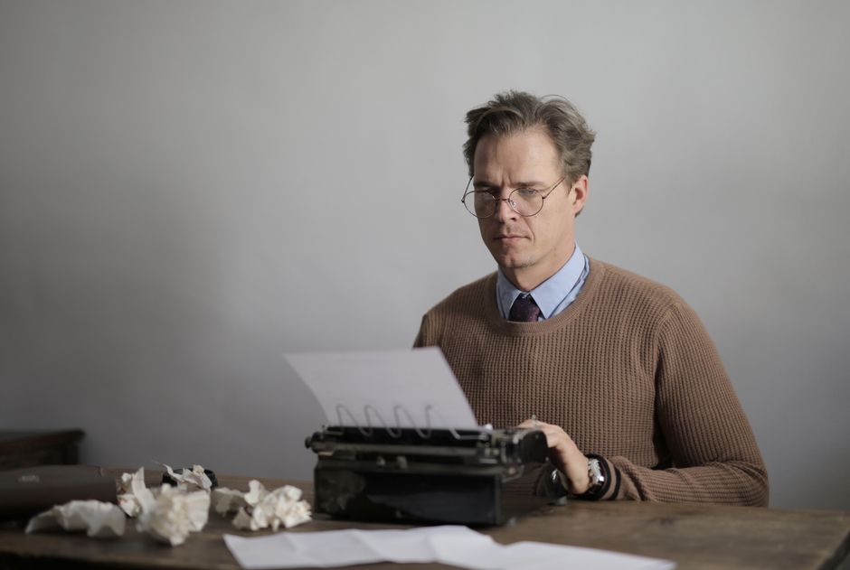Cheap Essay Writing Service Review 2026: Safe Budget Picks 3 Man concentrating on writing at a desk with a vintage typewriter surrounded by crumpled paper.
