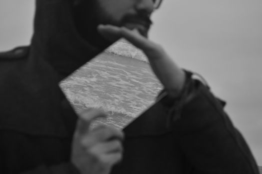 Creative black and white portrait with ocean waves reflected in a mirror held by a person.