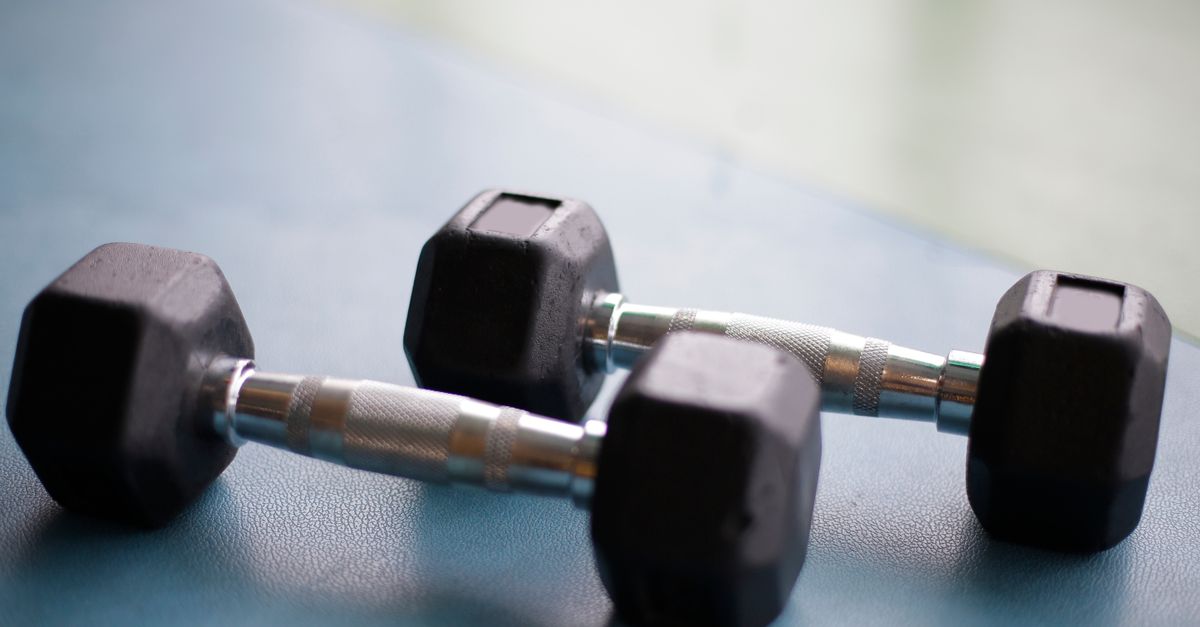 Black woman lifting free weights dumbbells in gym — free weights vs machines for women