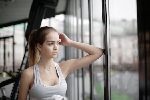 Young woman in sportswear gazing thoughtfully out of a gym window, embodying fitness and wellness.