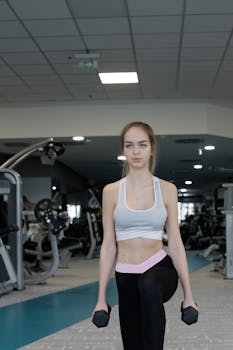 A young woman performs lunges with dumbbells in a modern gym setting.
