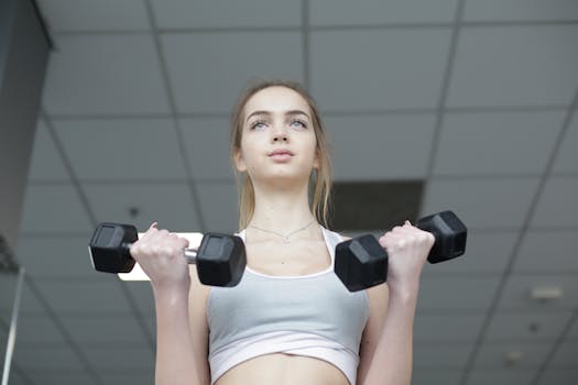 Focused young woman lifting dumbbells in an indoor gym setting.