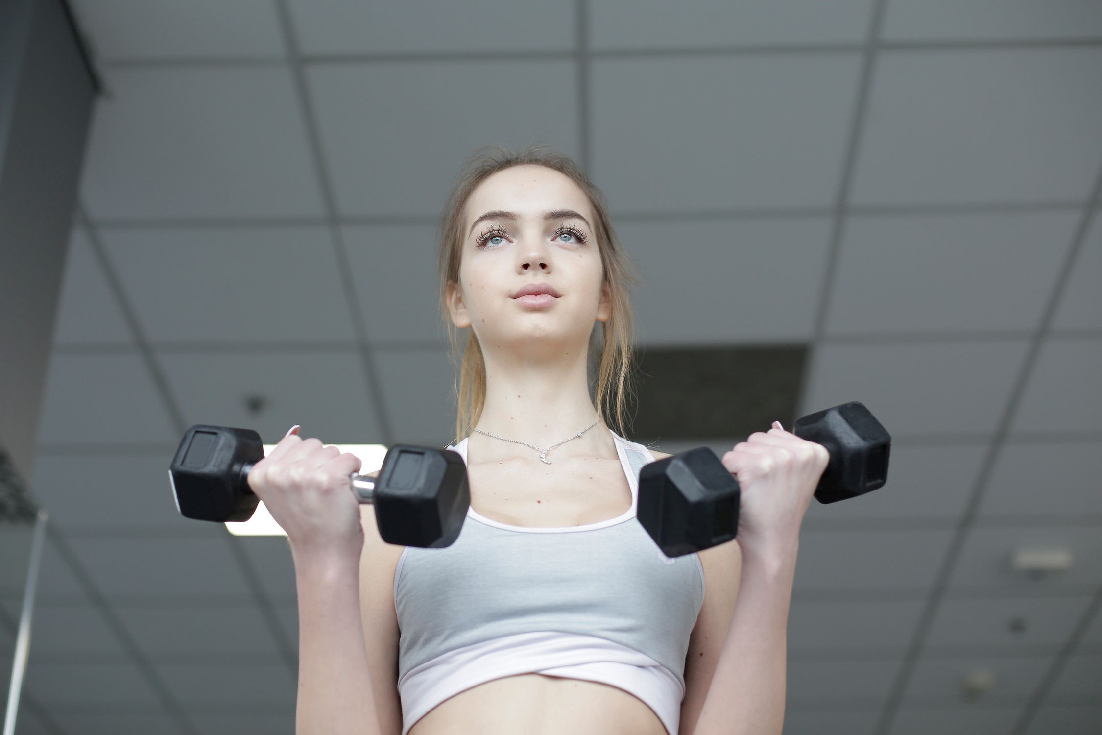 Mulher realizando exercício de musculação com halteres, com postura correta e ambiente clínico.