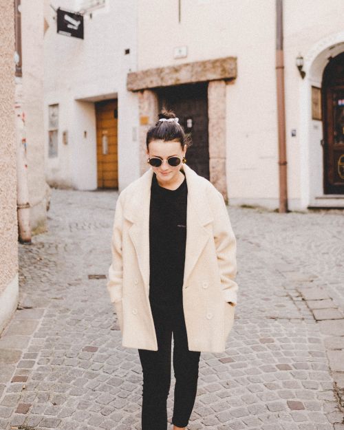 Free Fashionable woman in beige coat and sunglasses strolling through historic Salzburg street. Stock Photo
