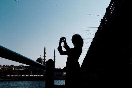 Silhouette of a person photographing Istanbul's skyline from a bridge with mosques in the background.