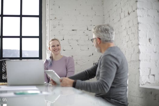 Two colleagues engaging in conversation, using technology in a modern office space.