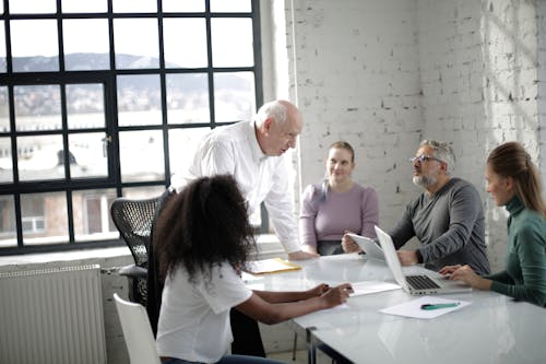 Serious multiethnic colleagues gathering around table with laptop and documents and discussing details of business project while working together in light modern office