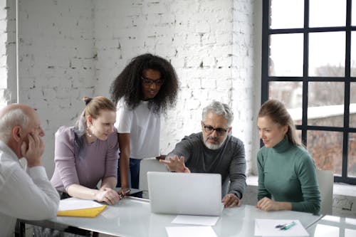 Free Group of serious multiracial colleagues sitting together at table near laptop and discussing details of project while working in spacious modern workspace Stock Photo