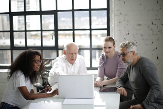 A diverse group of professionals collaborating around a laptop in a modern office space.