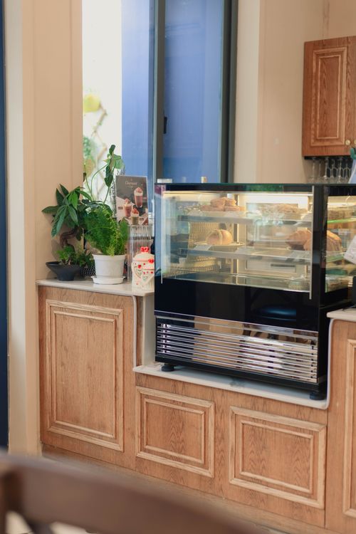 Free Bright and inviting cafe corner with pastries in display case and potted plants for decor. Stock Photo