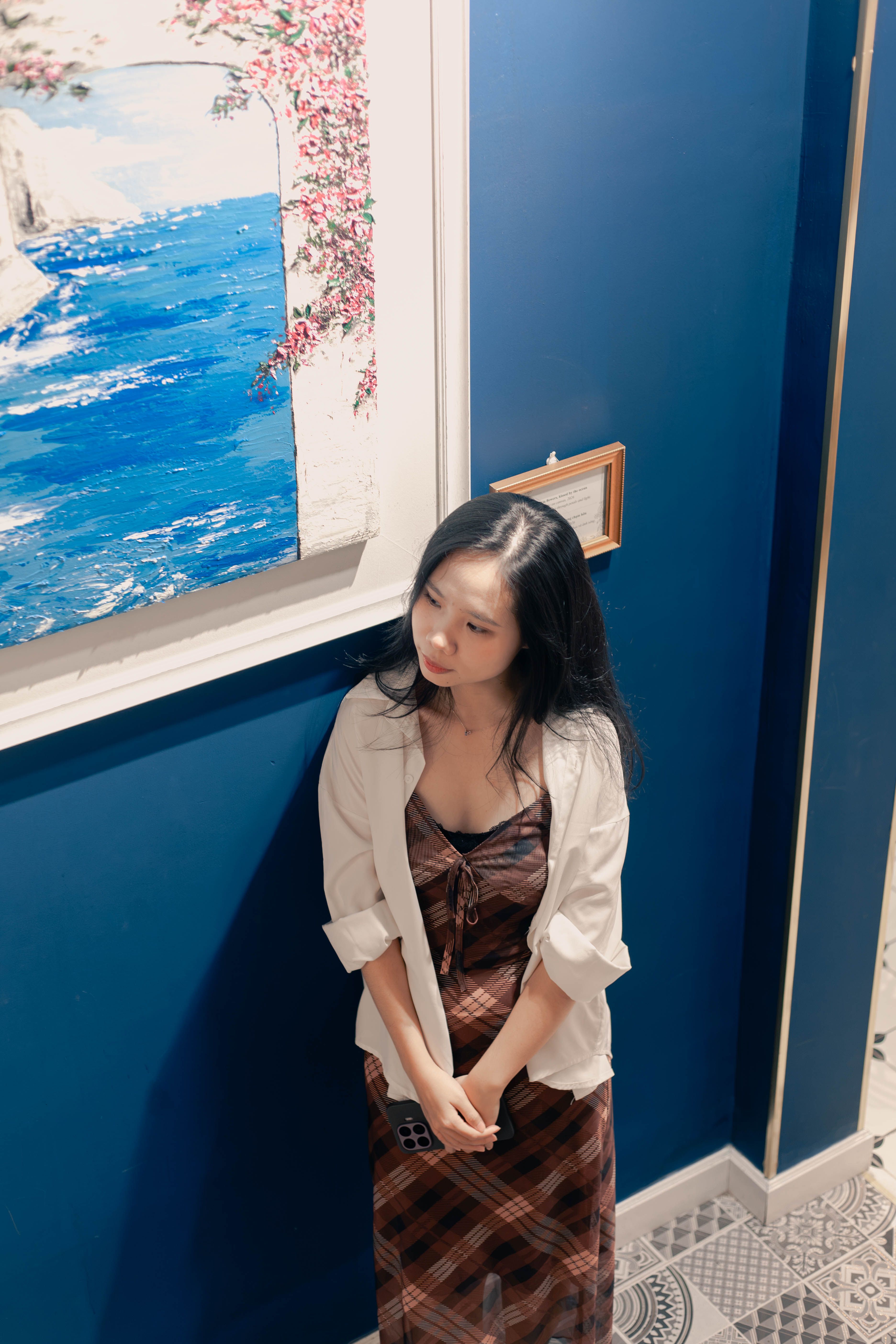 Young woman in a gallery, contemplating art, dressed stylishly, with muted tones.