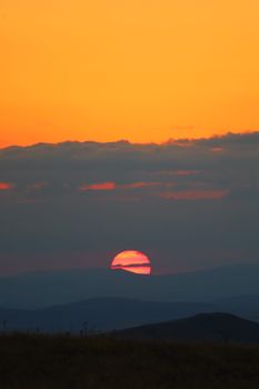 A picturesque sunset with an orange sky and dark hills in silhouette, creating a serene atmosphere.