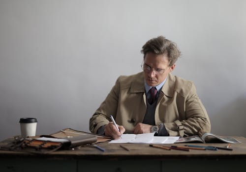 Focused male executive doing paperwork drinking takeaway coffee against gray wall in room