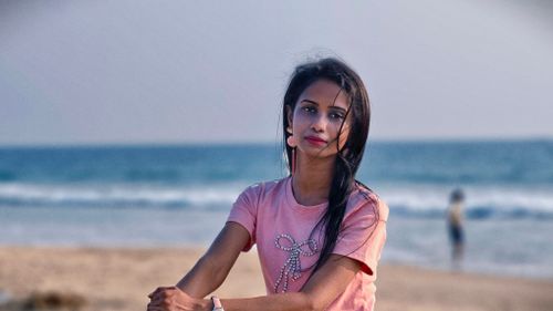 Free Portrait of a young woman on a sandy beach with ocean waves in the background. Stock Photo