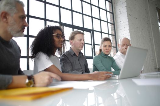 From below of focused multiracial colleagues of different ages in casual wear surfing netbook while making project together in light workplace