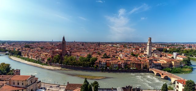 Stunning aerial view of Verona cityscape, featuring the Adige River winding through historic architecture under a clear blue sky.