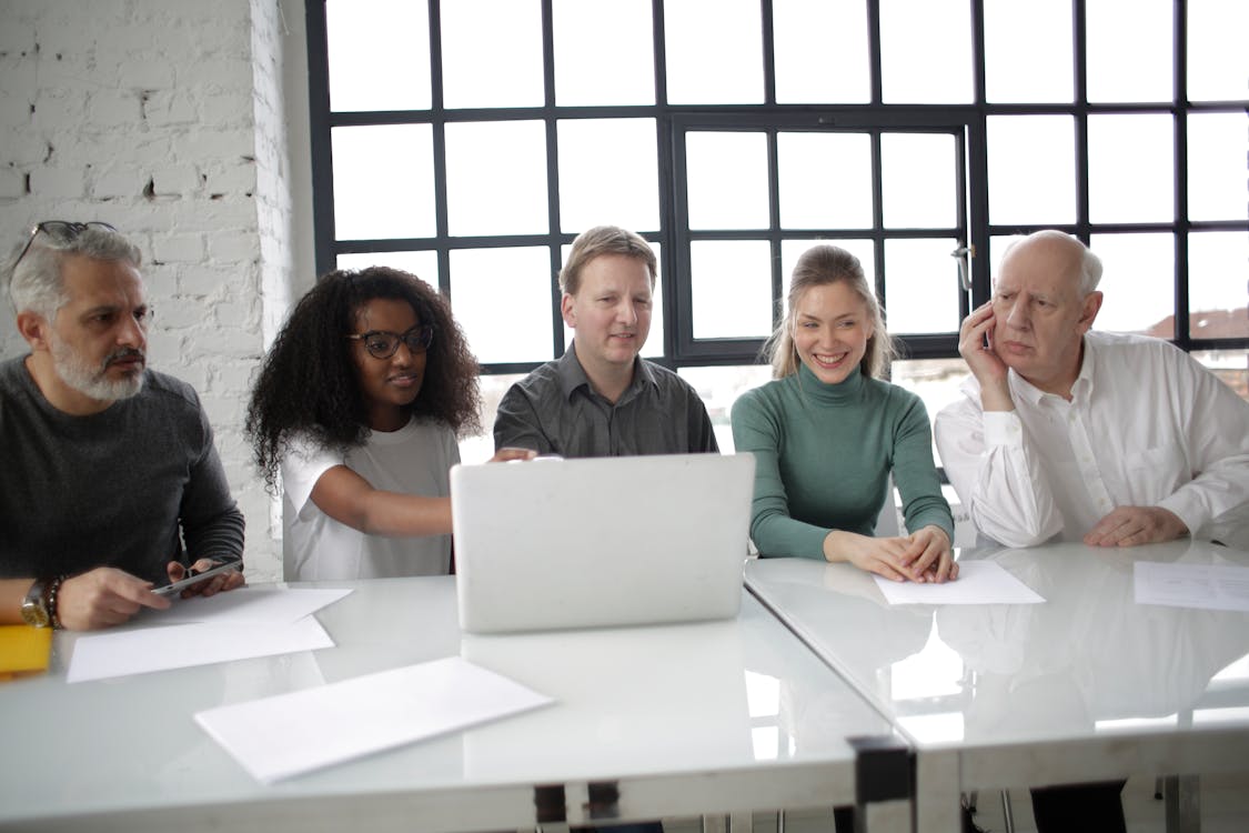 Free Group of multiracial coworkers of different ages discussing details of project while using computer at table in modern workplace Stock Photo