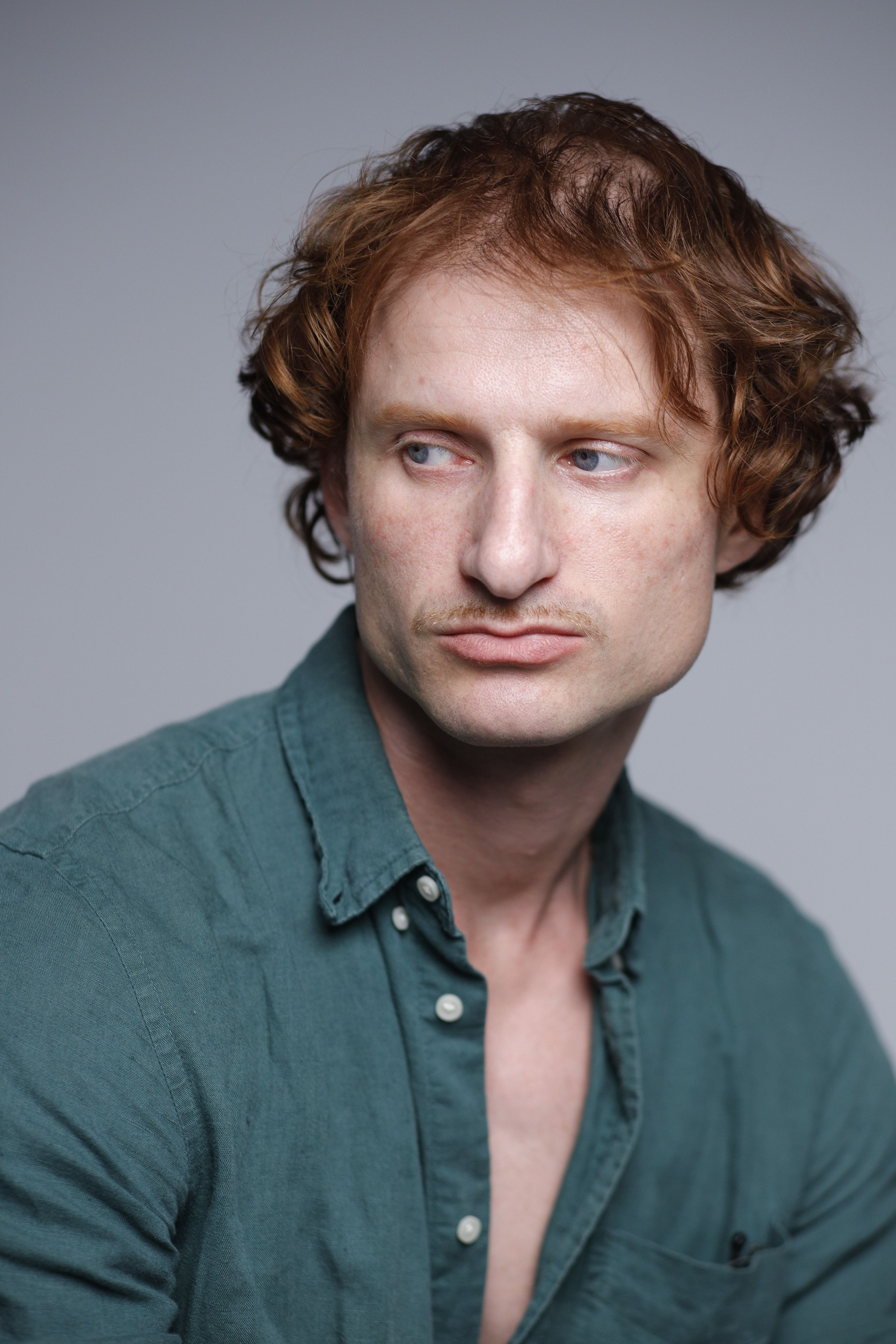 A thoughtful man in a green shirt gazes to the side in this indoor portrait.