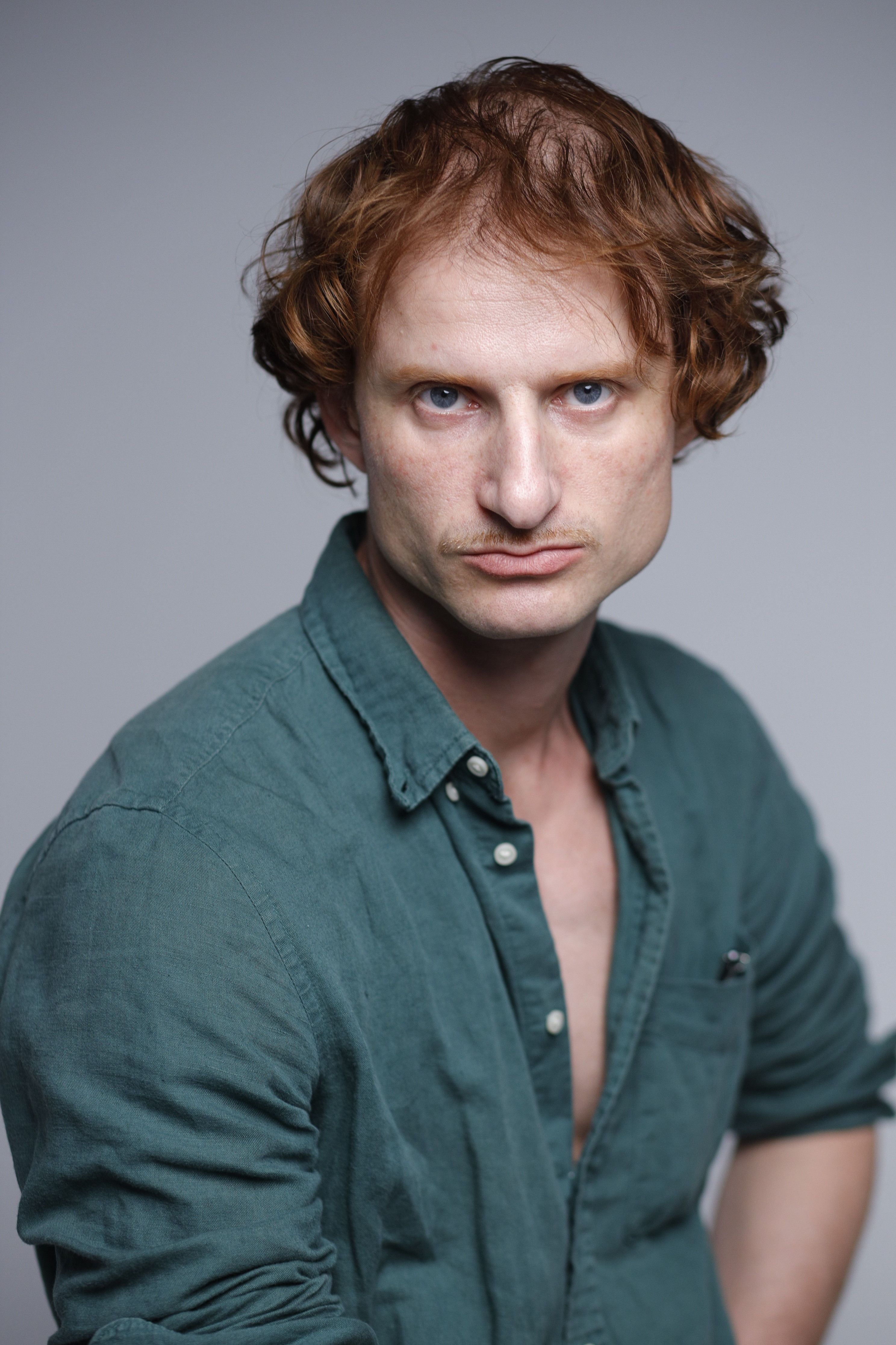 Close-up portrait of a man with ginger hair wearing a green shirt, studio setting.