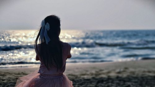 Free A woman with long hair and white bow gazing at the sunset over the ocean waves on a tranquil beach. Stock Photo