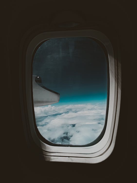 Porthole view of blue sky with fluffy white clouds and airplane turbine 