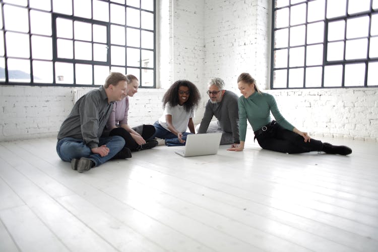 Cheerful Diverse People Working On Project Together At Laptop On White Floor In Spacious Room