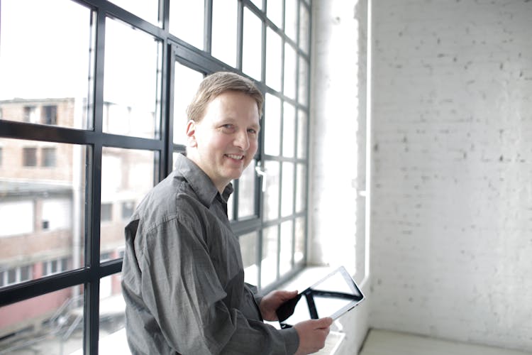 Happy Male Manager With Tablet Near Window In Spacious Workspace