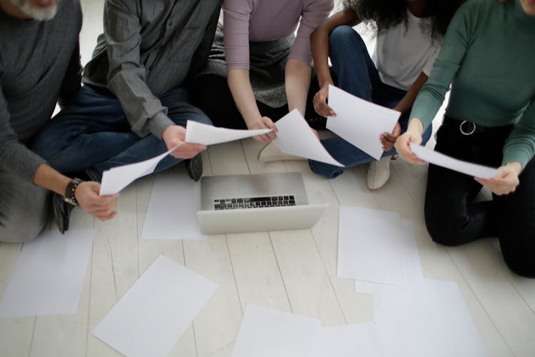 From Above Multiracial Colleagues Working With Papers And Laptop On Floor In Office