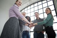 From below of happy diverse coworkers in casual clothing joining hands together while having training in spacious light office