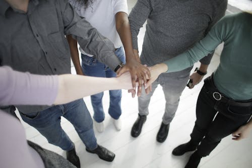 Free From above of faceless diverse coworkers wearing casual outfits stacking hands together while gathering in modern office at daytime Stock Photo