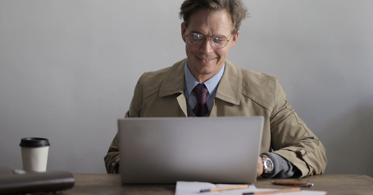 A well-dressed person on a laptop, with hands covered in clay or paint, looking content