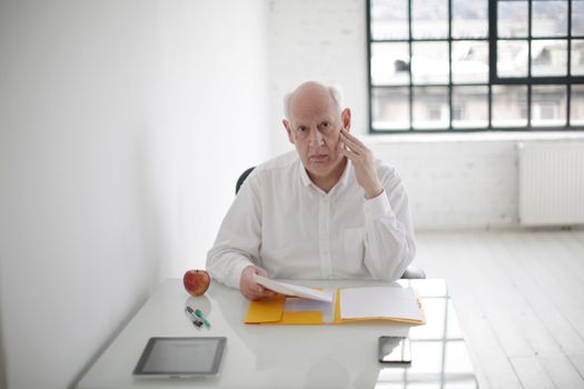 在现代办公室里，一位年长的商人坐在办公桌前，思考着文件内容