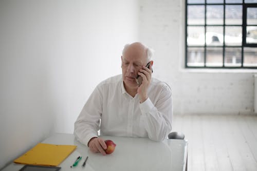 Thoughtful senior man speaking on smartphone in light office