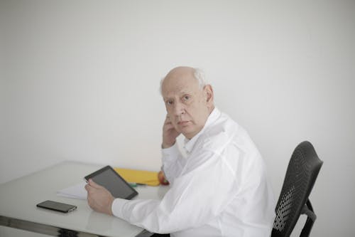 Side view of serious mature man in formal wear looking at camera while surfing tablet working on project in modern office